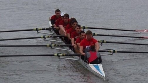 A rowing shell of 8 mens members rowing.